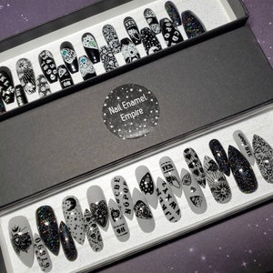 May include: Two sets of black and white press-on nails with various designs, including a Ouija board, a heart, a crescent moon, and the words "GOOD BYE", "YES", "ZAXMA", "CDE", "NOPOP", "4", "67890", and "ON".