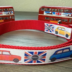 May include: Red dog collar with a white ribbon featuring illustrations of Mini Coopers and Union Jack flags. The collar has a red plastic buckle. Two red toy London buses are in the background.
