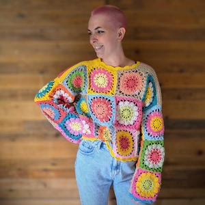 May include: A vibrant crochet sweater with a patchwork design and floral patterns. The sweater uses a variety of colours, such as yellow, pink, blue, and green. The sleeves are long and flared, and the neckline has a scalloped edge.