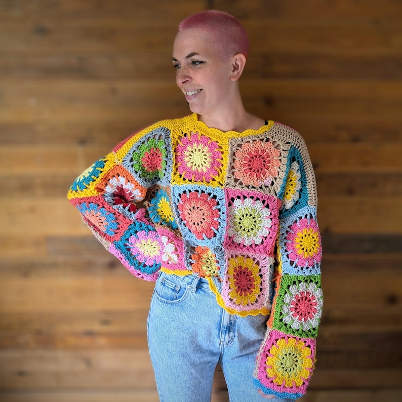 Puede incluir: Un colorido su&eacute;ter de ganchillo con un dise&ntilde;o de patchwork y motivos florales. El su&eacute;ter incorpora varios colores, incluyendo amarillo, rosa, azul y verde. Las mangas son largas y acampanadas, y el cuello es festoneado.