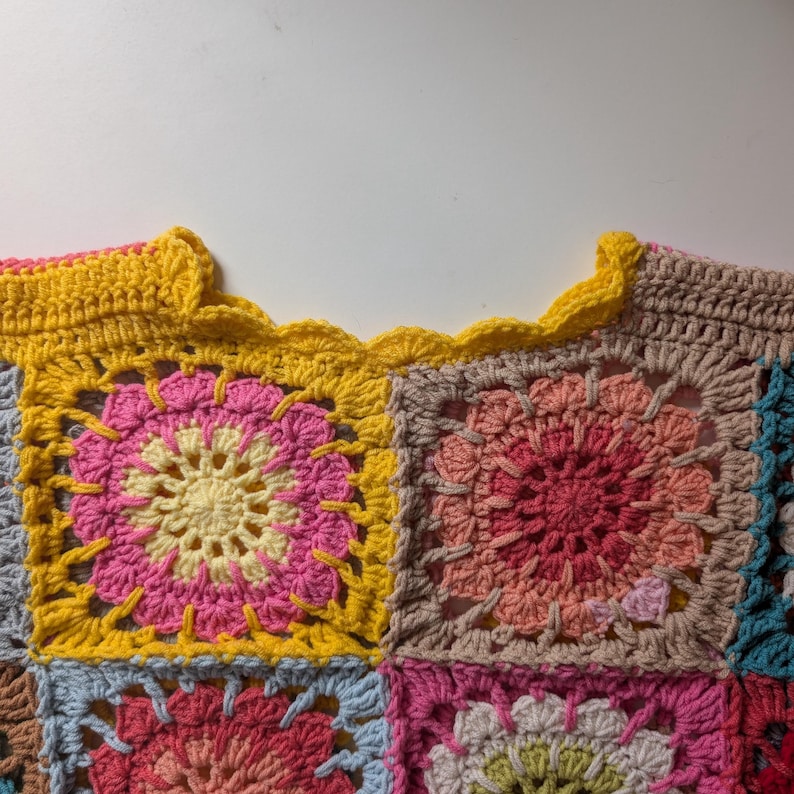 Puede incluir: Top de ganchillo hecho a mano con un dise&ntilde;o de patchwork. La parte superior est&aacute; compuesta por motivos cuadrados en varios colores, incluyendo amarillo, rosa, rojo y marr&oacute;n. El escote tiene un borde festoneado en amarillo brillante.