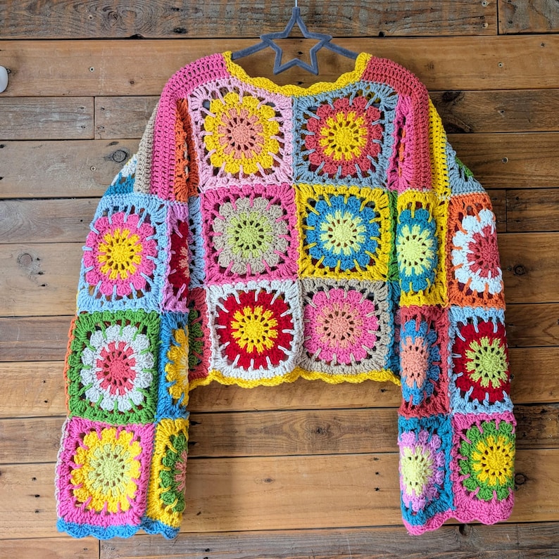 Puede incluir: Un colorido su&eacute;ter de crochet hecho a mano con un dise&ntilde;o de patchwork de cuadrados florales en tonos rosa, amarillo, azul, verde y rojo. El su&eacute;ter tiene mangas largas y un escote festoneado, perfecto para un look bohemio &uacute;nico.