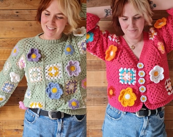 May include: Two women wearing crocheted cardigans with floral designs. One cardigan is green with white and pink flowers, the other is pink with orange, yellow, and white flowers. Both women are wearing blue jeans.