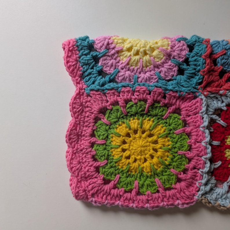 Puede incluir: Primer plano de un cuadrado de ganchillo colorido y hecho a mano. El cuadrado presenta un borde rosa, que rodea un dise&ntilde;o central de amarillo, verde y rosa. El trabajo de ganchillo es detallado, con puntadas visibles y una superficie texturizada. La est&eacute;tica general es vibrante y artesanal.