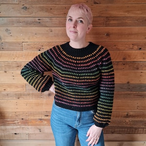 May include: A black crochet sweater with rainbow stripes. The sweater has a round neckline and long sleeves.