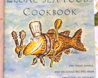 May include: The cover of a cookbook titled "The New Legal Sea Foods Cookbook". The cover features a cartoon illustration of a fish wearing a chef's hat and holding a spoon. The background is a watercolor painting of a blue sky with white clouds.