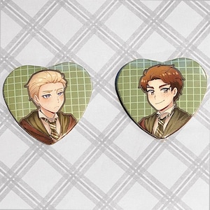 May include: Two heart-shaped pins with green and white checkered backgrounds. Each pin features a cartoon illustration of a young man with brown hair and a green and brown uniform.