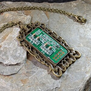 May include: A unique necklace featuring a green circuit board pendant set in an ornate, antique brass-colored frame. The pendant hangs from a matching chain, creating a distinctive tech-inspired accessory.