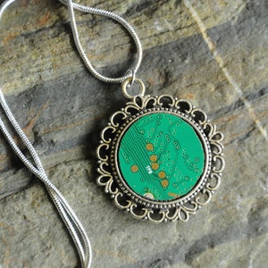 Puede incluir: Un collar de cadena de plata con un colgante redondo que presenta una placa de circuito verde dentro de un marco de filigrana de plata.