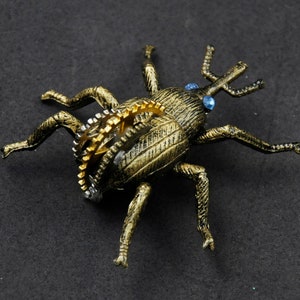 May include: A gold-colored, steampunk-style beetle with intricate gears and blue accents. The beetle is made of metal and has a detailed, textured surface.