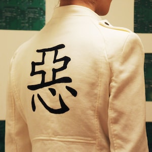 May include: Cream-colored jacket with a mandarin collar and shoulder epaulets. The back of the jacket features a large black Japanese Kanji symbol. The jacket is a neutral color and has a tailored fit.