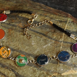 Puede incluir: Un collar hecho de placas de circuito recicladas. El collar tiene un cordón de cuero negro y detalles metálicos dorados. Las placas de circuito son de varios colores, incluyendo rojo, naranja, verde, azul y morado.