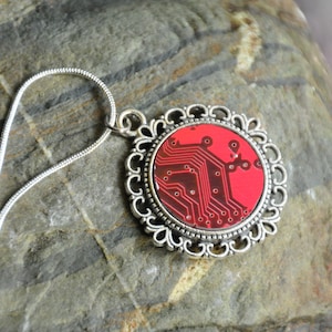Puede incluir: Un collar de cadena de plata con un colgante de placa de circuito rojo y negro en un marco de filigrana de plata.