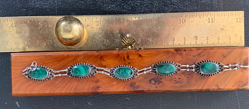 silver bracelet set with oval cabochon malachite stones within a burr-wood presentation case .