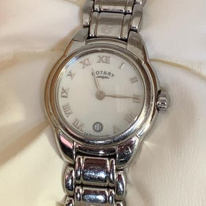 May include: A silver Rotary wristwatch with a white face and Roman numeral hour markers. The watch has a date display at the 6 o'clock position and a silver link bracelet. The watch face reads "Rotary".