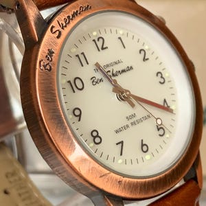 K&ouml;nnte beinhalten: Eine Ben Sherman Uhr mit braunem Lederarmband und kupferfarbenem Geh&auml;use. Das Zifferblatt der Uhr ist cremefarben mit schwarzen Ziffern und Zeigern. Die Uhr ist wasserdicht bis zu 50 Meter.