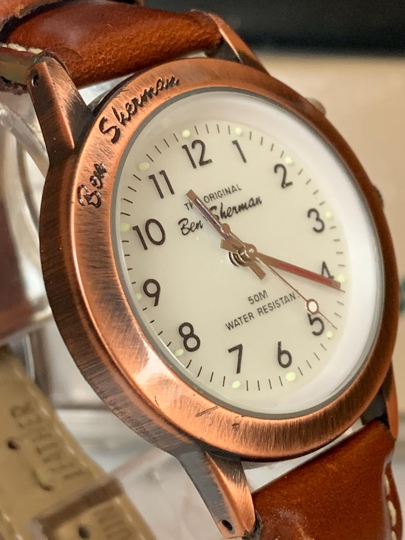 K&ouml;nnte beinhalten: Eine Ben Sherman Uhr mit braunem Lederarmband und kupferfarbenem Geh&auml;use. Das Zifferblatt der Uhr ist cremefarben mit schwarzen Ziffern und Zeigern. Die Uhr ist wasserdicht bis zu 50 Meter.