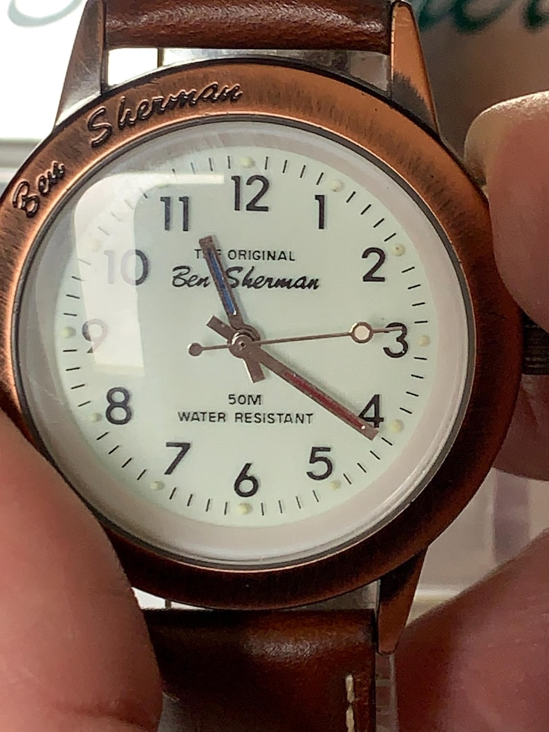 K&ouml;nnte beinhalten: Eine Ben Sherman-Uhr mit kupferfarbenem Geh&auml;use und braunem Lederarmband. Das cremefarbene Zifferblatt hat schwarze Ziffern und Zeiger. Der Text "THE ORIGINAL Ben Sherman" und "50M WATER RESISTANT" sind zu sehen.