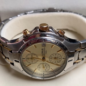 May include: A silver and gold Lorus Chronograph watch with a gold face. The watch has three sub-dials, a date display, and gold accents on the bezel and crown. The watch strap is silver with gold-toned links.