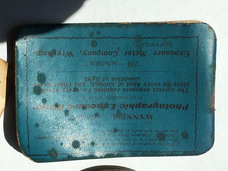 Op de afbeelding: Een blauwe vintage fotografische belichtingsmeter met tekst. De tekst bevat "WYNNE'S Photographic Exposure Meter" en "Exposure Meter Company, Wrexham". Het is ontworpen om de juiste belichting te bepalen.