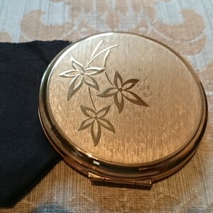May include: A gold compact mirror with a floral design. The mirror has a brushed gold finish and a hinged lid.