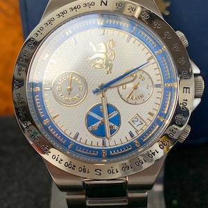 Puede incluir: Un reloj de pulsera plateado con esfera blanca, detalles azules y correa de acero inoxidable. El reloj presenta un emblema dorado y el texto "SCOTLAND FOREVER". Incluye una pantalla de fecha y varias subesferas.