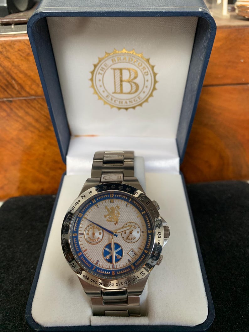 Puede incluir: Reloj de pulsera de acero inoxidable con esfera blanca, detalles azules y esfera detallada. El reloj est&aacute; en una caja azul con el logotipo "The Bradford Exchange". Cuenta con una pantalla de fecha y una correa de metal.