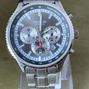 May include: A silver men's chronograph wristwatch with a black face and white markings. The watch has a tachymeter scale around the outer edge of the face. The watch face also includes the words "SEKONDA" and "50 m res".