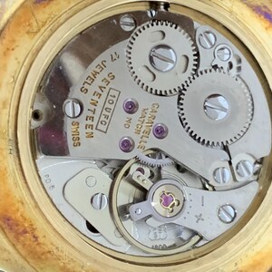 May include: Close-up of the back of a gold-tone wristwatch with a silver-tone face. The watch face has the text "10 UFC, SEVENTEEN JEWELS, SWISS" and "GARAVELLE WATCH NO."