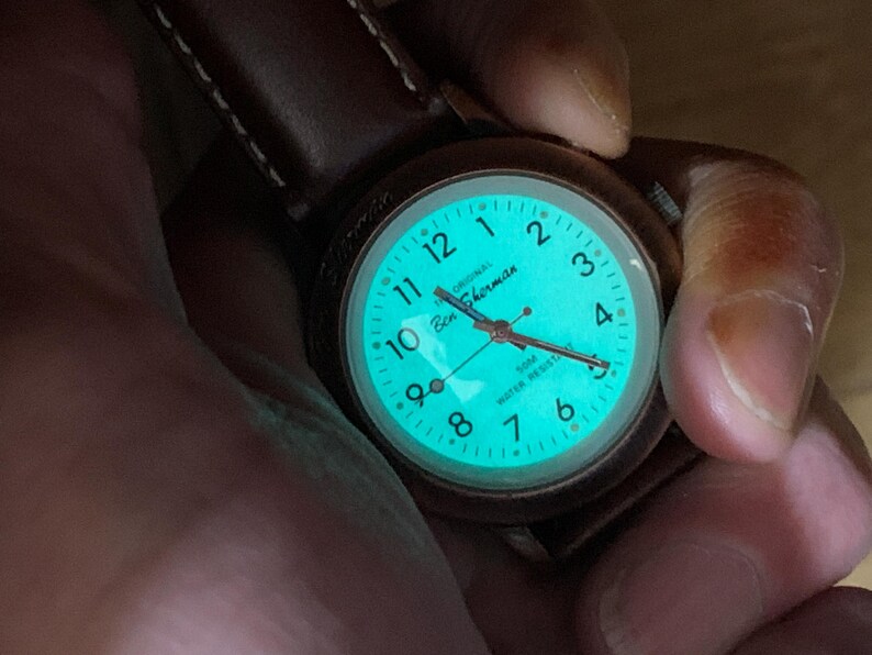 K&ouml;nnte beinhalten: Eine Ben Sherman-Uhr mit braunem Lederarmband. Das Zifferblatt leuchtet t&uuml;rkis und zeigt wei&szlig;e Ziffern und Zeiger. Die Uhr ist wasserdicht bis 50m.