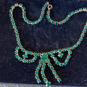 Peut inclure: Un collier de strass vert avec un design en forme de nœud. Le collier est composé de petits strass ronds sertis dans du métal doré.