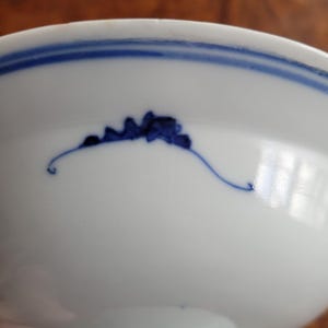 May include: White ceramic bowl with a blue floral design and a blue stripe around the rim. The bowl has a smooth, glossy finish and a simple, elegant design. The blue floral design is hand-painted.
