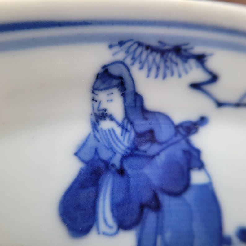 May include: A close-up of a white ceramic bowl with a blue and white illustration. The illustration depicts a figure with a long beard and traditional clothing. The bowl has a blue rim.