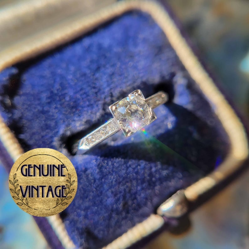 May include: A vintage engagement ring with a square-cut diamond set in a silver band. The ring is in a blue velvet ring box.