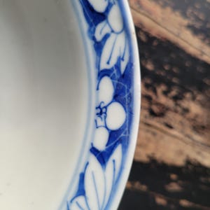 May include: A white ceramic bowl with a blue floral border. The border features stylized white flowers and leaves against a blue background. The bowl's interior is plain white, and the design is a classic, elegant style.