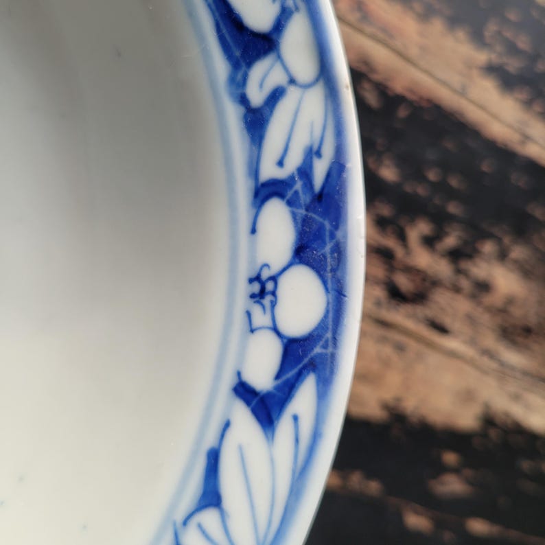 May include: A white ceramic bowl with a blue floral border. The border features stylized white flowers and leaves against a blue background. The bowl's interior is plain white, and the design is a classic, elegant style.