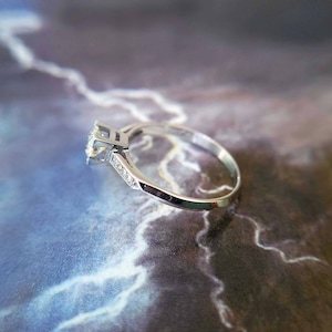 May include: A silver engagement ring with a single round diamond and smaller diamonds set in the band.