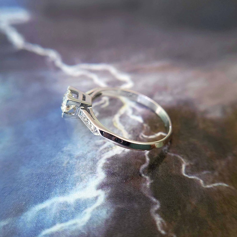 May include: A silver engagement ring with a single round diamond and smaller diamonds set in the band.
