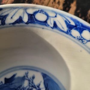 May include: A white ceramic bowl with a blue floral border. The bowl's rim features a repeating pattern of stylized leaves and flowers in a deep blue hue. The interior of the bowl has a blue and white design.