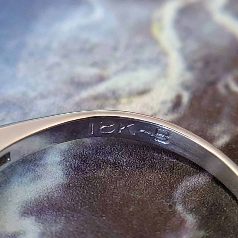 May include: Close-up of the inside of a silver ring with the inscription "18K" on the band.