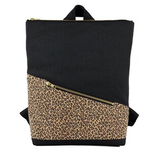 Könnte beinhalten: Schwarzer Rucksack mit diagonalem Leopardenmuster und goldenem Reißverschluss. Die Tasche hat einen oberen Griff und verstellbare Schultergurte. Der Rucksack ist aus strapazierfähigem Stoff gefertigt.
