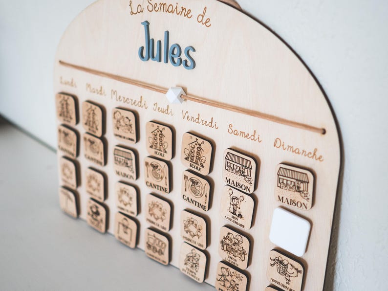 May include: Wooden weekly calendar with the text "La Semaine de Jules". The calendar has wooden square tiles with illustrations for each day of the week. The days of the week are written in French.
