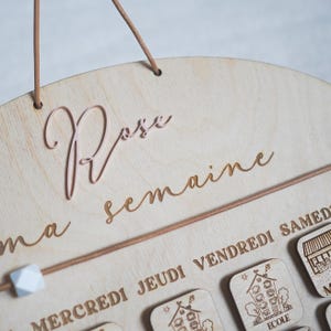 May include: A wooden wall calendar with the words "Ma semaine" and "Rose" written on it. The calendar has days of the week labeled in French: "Mercredi", "Jeudi", "Vendredi", and "Samedi".