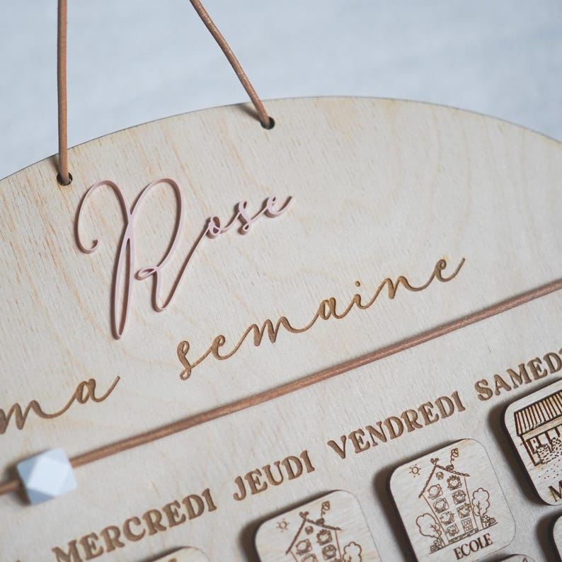 May include: A wooden wall calendar with the words "Ma semaine" and "Rose" written on it. The calendar has days of the week labeled in French: "Mercredi", "Jeudi", "Vendredi", and "Samedi".