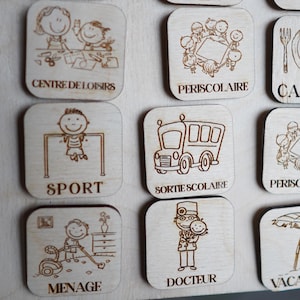 May include: Wooden square tiles with illustrations and French text. The tiles feature images of a school bus, a doctor, a child playing sports, a child doing chores, a child at a daycare, a child at a school, and a child on vacation.