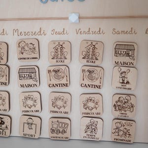 May include: Wooden calendar with engraved icons and French text. The calendar features various activity icons, including school, home, and dining, with the days of the week written across the top. The calendar is designed for educational or organizational purposes.