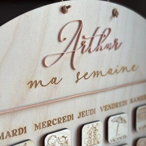 May include: A wooden weekly planner with the name "Arthur" and the text "ma semaine" (my week) in cursive script. The planner has days of the week labeled in French: Mardi, Mercredi, Jeudi, Vendredi, Samedi, and Dimanche.