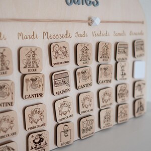 May include: Wooden children's calendar with engraved days of the week and activity icons. Includes labels like "School," "Canteen," and "Sports." The calendar has a light wood finish and a decorative top with the word "Dates."