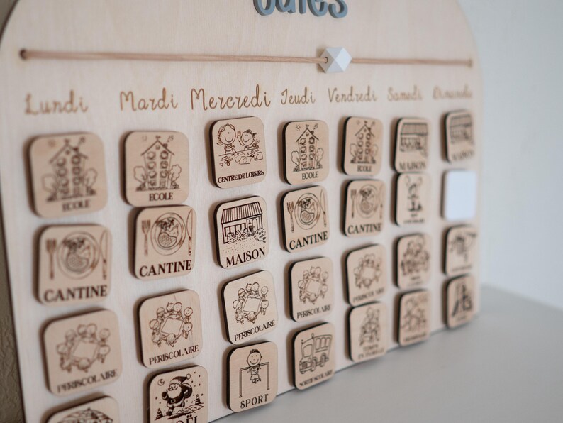 May include: Wooden children's calendar with engraved days of the week and activity icons. Includes labels like "School," "Canteen," and "Sports." The calendar has a light wood finish and a decorative top with the word "Dates."