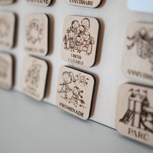May include: Wooden square plaques with etched illustrations and text. The plaques depict family activities, including a family gathering, a walk, and a playground. The text includes the words "VISITER LA FAMILLE", "PROMENADE", and "PARC".